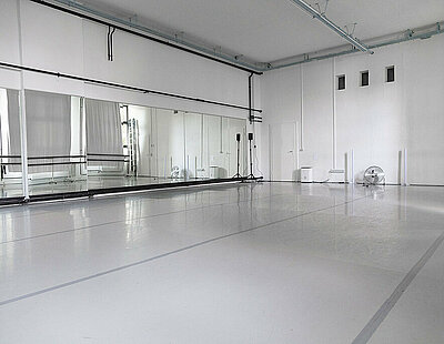 Das Studio 29 in Berlin mit weißem Tanzboden und einer verspiegelten Wand. Gegenüber sind Fenster mit weißen Vorhängen zu sehen.